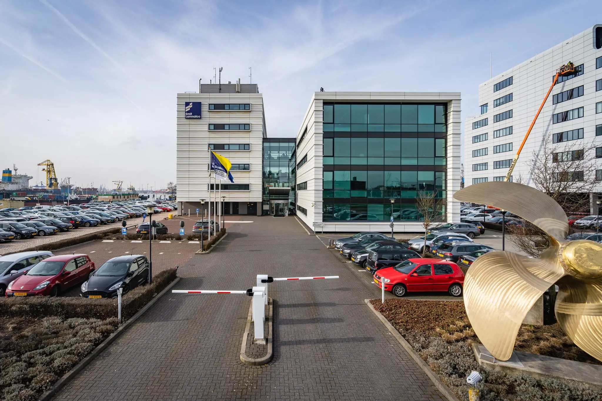 Kantoorgebouw van STC Group aan de Waalhaven in Rotterdam met parkeerterrein, vlaggenmast en grote scheepsschroef op de voorgrond.